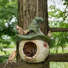 a bird house with birds sitting on top of it next to a tree trunk and fence