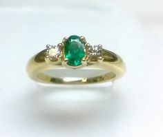 an emerald and diamond three stone ring on a white surface with two diamonds in the middle