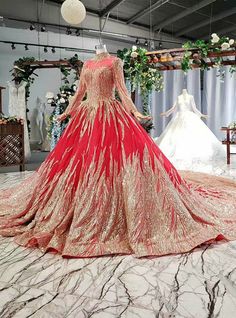 a red and gold wedding gown on display in a room with white flowers hanging from the ceiling