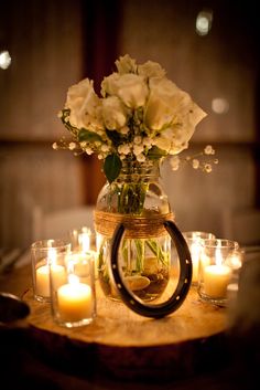 a vase filled with white flowers sitting on top of a wooden table next to candles