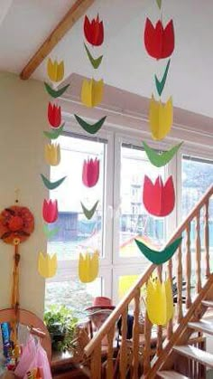 paper tulips hanging from the ceiling in front of a window and staircase leading up to a second floor