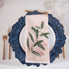 a place setting with an olive branch on the napkin and gold cutlery, along with silverware