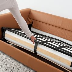 a person reaching for the mattress on top of a bed frame in a living room