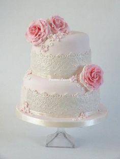 a three tiered wedding cake with pink roses on the top and bottom, sitting on a stand