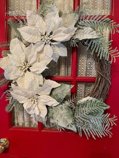 a wreath with white poinsettis and greenery hangs on a red door