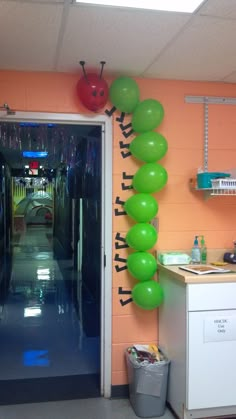 a hallway decorated with green balloons and ladybugs on the wall next to an open door