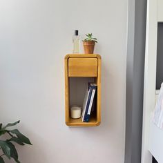 a wooden shelf with books and plants on it next to a white wall in a bedroom