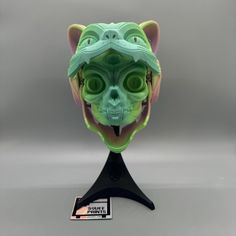 a green mask with an animal's head on top of a black stand against a gray background