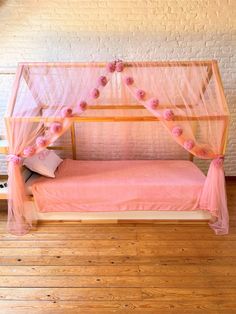 a pink bed with sheer curtains and flowers on the headboard, in front of a brick wall