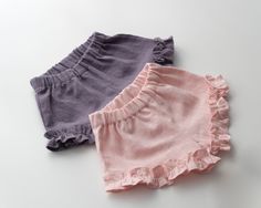 three baby girls'ruffle blooming shorts on a white surface, one in pink and the other in purple