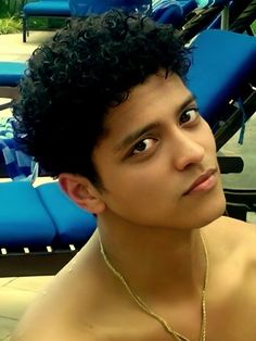 a shirtless young man sitting next to blue lounge chairs and looking at the camera