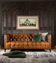 a leather couch in front of a wooden paneled wall with a framed photo on it