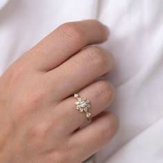 a woman's hand wearing a gold ring with three small white flowers on it