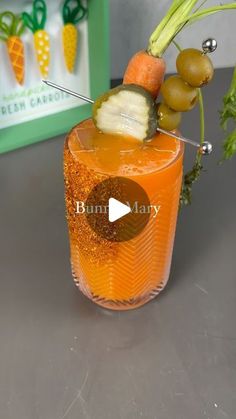 a glass filled with orange liquid and garnish on top of a table next to a green box