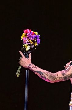 a man with tattoos holding flowers in his right hand while standing next to a microphone