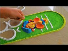 a child's hand holding scissors over a green rug with orange and white decorations on it