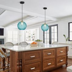 a large kitchen with wooden cabinets and white counter tops, two blue glass pendant lights hanging over the island