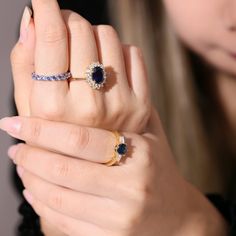 a woman holding two different rings on her finger and wearing a ring with an oval shaped blue stone