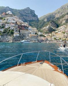 a boat traveling on the water near a city with mountains in the backgroud