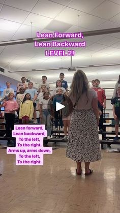 a woman standing in front of a group of people on a hard wood floor next to a microphone