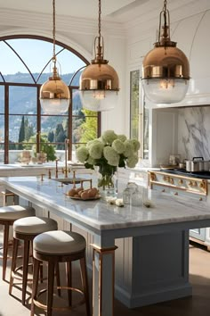 a large kitchen with marble counter tops and gold pendant lights hanging from the ceiling above it