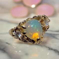 This stunning ring is made of 14k solid gold and has a pear shape high quality natural fire opal that captures attention with its mesmerizing play of colors. On each side of the opal, there are two brilliant cut Moissanites, adding a touch of elegance and sparkle. The design of the ring features organic shapes, giving it a unique and artistic feel. The shiny finish of the gold enhances its beauty and makes it stand out even more. This ring is truly one of a kind, with its sea life-inspired desig Unique Gemstones, Organic Shapes, Ring Size 7, Custom Rings, Ethiopian Opal, Fire Opal, Rings Statement, Costume Jewelry, Etsy Store