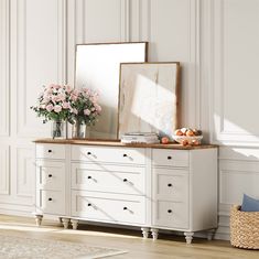 a white dresser with flowers and vases on it in front of a large mirror