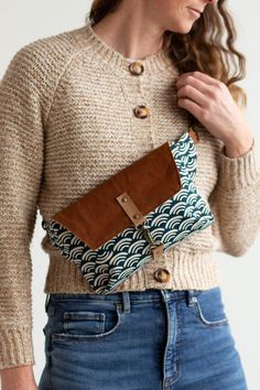 a woman in jeans and a sweater holding a brown purse with an interesting design on it