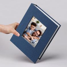 a hand holding an open blue book with a photo on the front and bottom cover