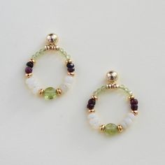 Our white opal, ruby, and peridot earrings are packed with gemstones.  A unique July, August or October birthstone gift OR 14th, 15th, 16th or 40th-anniversary gift.  The 14k gold-filled post earrings feature a peridot bead at the base and top of the hoop, complemented by white opals, gold-plated brass, and contrasting red rubies.  The pair is lightweight and long-lasting.  A lovely personal treat or gift for your wife, mom, or friend.   The jewelry arrives wrapped for easy gifting and includes May Birthstone Hoop Gemstone Jewelry, Green Gemstone Round Bead Earrings, Green Gemstone Earrings With Round Beads, Green Small Hoop Sterling Silver Jewelry, Green Sterling Silver Small Hoop Jewelry, Dainty Sterling Silver Earrings With Gemstone Accents, Hoop Jewelry With May Birthstone, Hoop May Birthstone Jewelry Gift, Hoop Jewelry With May Birthstone For Gifts