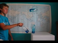 a young boy holding two water bottles in front of a world map on the wall