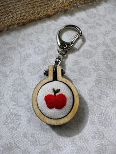 a wooden keychain with an embroidered apple on the front and bottom, hanging from a hook