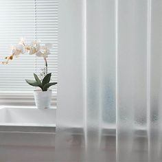 a white vase with flowers in it sitting on a window sill next to a curtain