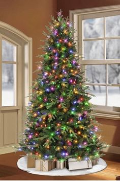 a christmas tree with multicolored lights in a living room next to a window