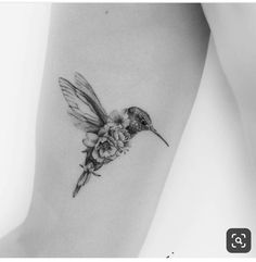 a small hummingbird with flowers on its back leg tattoo by the talented artist jane