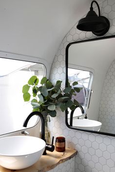 a white sink sitting under a bathroom mirror next to a wooden counter with a plant in it