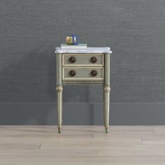 a small table with two drawers and a marble top in front of a gray wall