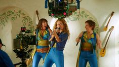 three women singing into microphones while standing in front of a video camera and recording equipment