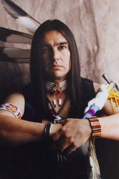 a man with long hair and feathers on his arm