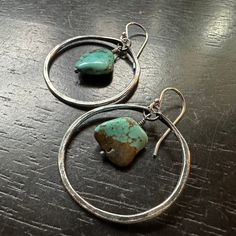 Our December birthstone is TURQUOISE, and once again we have some lovely gemstones to use in our earrings and necklaces! Our small, forged and hammered Sterling Silver hoops are paired with some beautiful, smooth little chunks of raw Turquoise, full of earthy colors swirling in and around those great teals!1 1/4" in diameter, Sterling Silver hoops and sterling silver earwires.*Due to the unique qualities of every Turquoise, the pair you receive may be slightly different from the ones pictured, but as they come from the same batch of gemstones they are all very consistent in size and coloration! Small Silver Hoop Earrings, Raw Turquoise, Color Swirl, Brass Hoops, Hammered Sterling Silver, December Birthstone, Earthy Colors, Sterling Silver Hoops, Silver Hoops