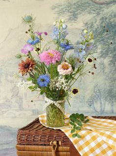 a vase filled with lots of flowers sitting on top of a wooden table next to a basket