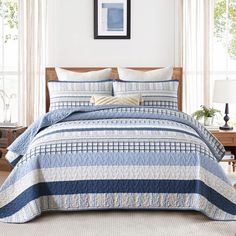 a bed with blue and white bedspread in a bedroom next to two windows