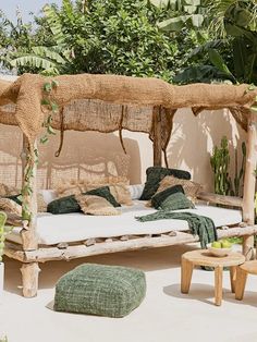 an outdoor day bed with pillows and blankets on it, surrounded by greenery in the background