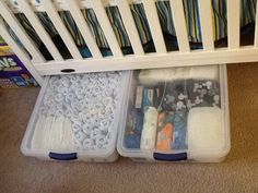 two plastic containers filled with sewing supplies under a crib