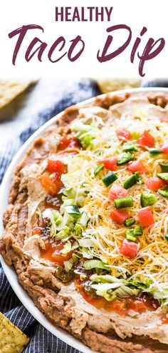 a taco dip on a plate with tortilla chips and salsa in the background