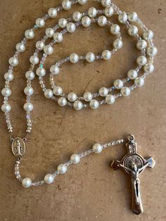 This Wedding Gift Rosary symbolizes the unity of marriage between the bride and groom and the union of the two becoming one in Christ. What great blessings it gives to that special couple and their new life together! This elegant pearl glass bead rosary was made handmade in the USA using 10mm White Pearl glass beads with Czech fire-polished AB crystal glass accent beads, and your choice of Our Father beads (pearl beads or Mother of Pearl Cross), your choice of rosary center and if you want metal end caps on the pearl beads.  A gorgeous 3" silver Benedictine crucifix completes the rosary beautifully. The length of the rosary hanging up is 31 inches from top to bottom. Comes in a velvet drawstring bag. White 8mm Beads Jewelry For Anniversary, White Hand-strung Wedding Necklaces, White Hand-strung Necklaces For Wedding, Hand-strung Pearl Wedding Necklaces, Hand-strung Pearl Necklaces For Weddings, Pearl White 8mm Beads Jewelry Gift, Pearl White Jewelry With 8mm Beads For Gift, Pearl White Jewelry With 8mm Beads As Gift, Elegant Pearl White Jewelry For First Communion