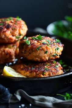 three crab cakes on a black plate with lemon wedges and parsley in the background