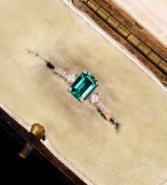 an emerald and diamond ring sitting on top of a box