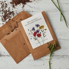 two greeting cards with wildflowers on them sitting next to some herbs and seeds