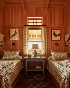 two beds in a room with wood paneling and pictures on the wall above them